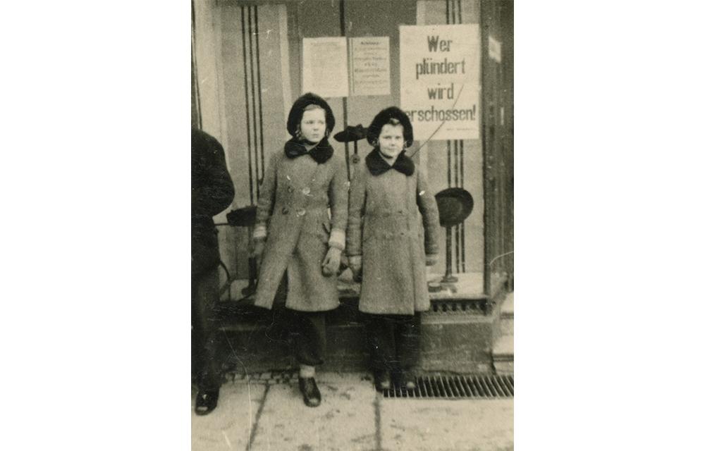Da die Mutter für das Festhalten der ersten Lebensmonate ihres dritten Kindes eine Kamera mitgenommen hatte, hielt sie zusätzlich Momente ihrer Flucht fest, indem sie ihre Töchter, wie hier in Primkenau im Januar 1945, vor Motiven platzierte, die sonst nicht hätten fotografiert werden dürfen.